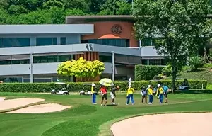 Golfers walking with caddies in front of Siam Country Club Old Course clubhouse in Thailand